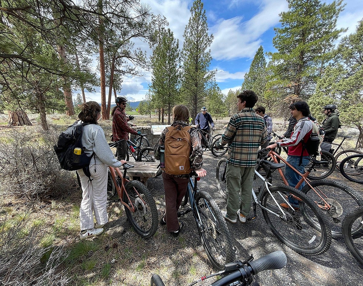 SCYP students, each with a bicycle, stand amongst trees around their instructor