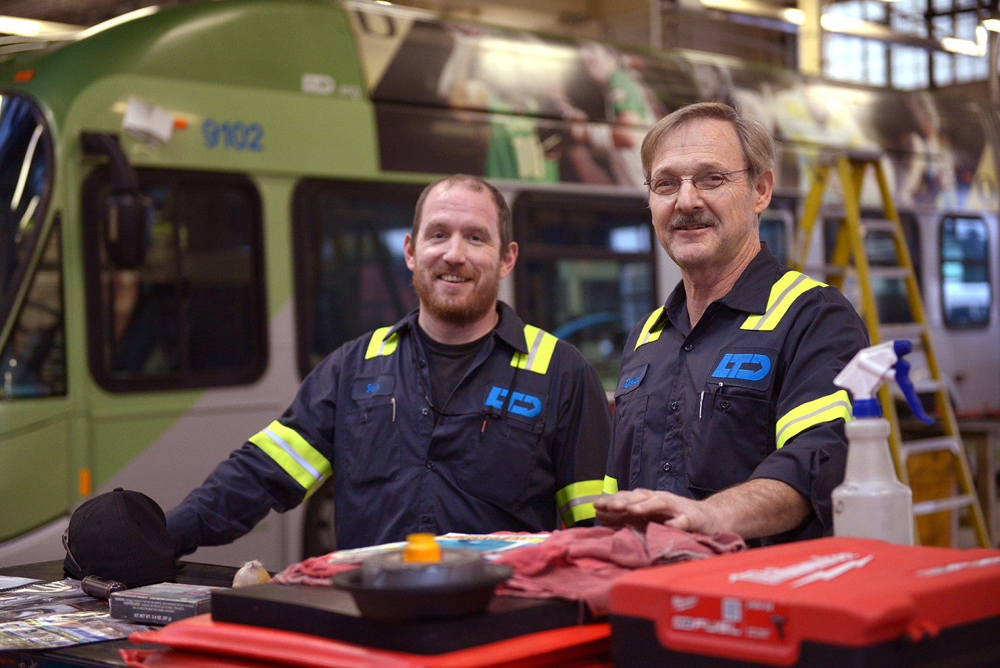 Two men in LTD employee uniforms smile in front of LTD bus