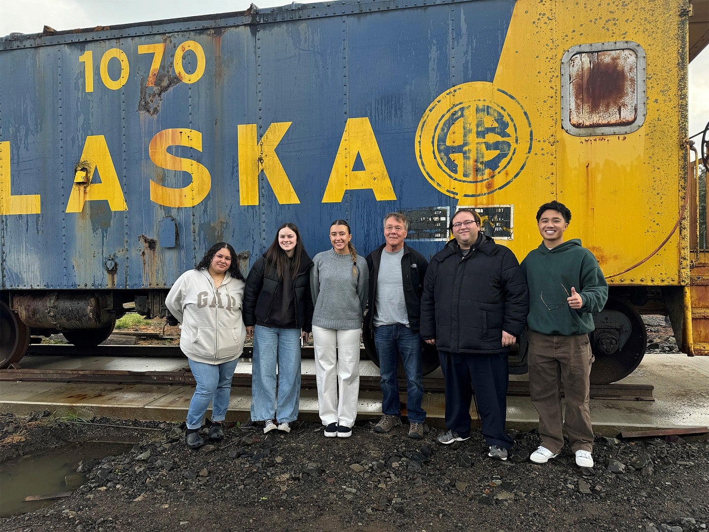 Six people stand in front of train and smile