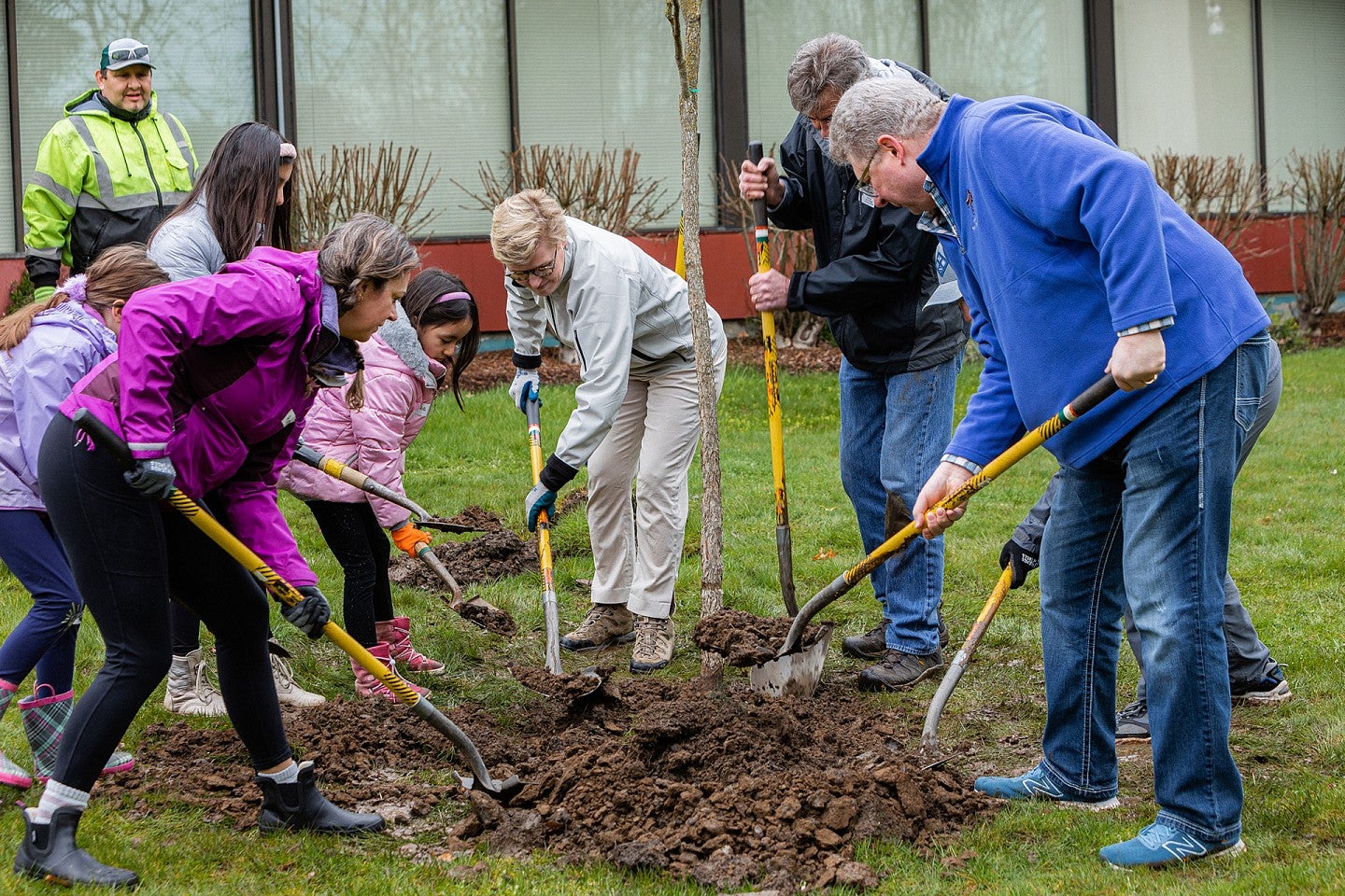 A group of adults and children shovel dirt to plant trees