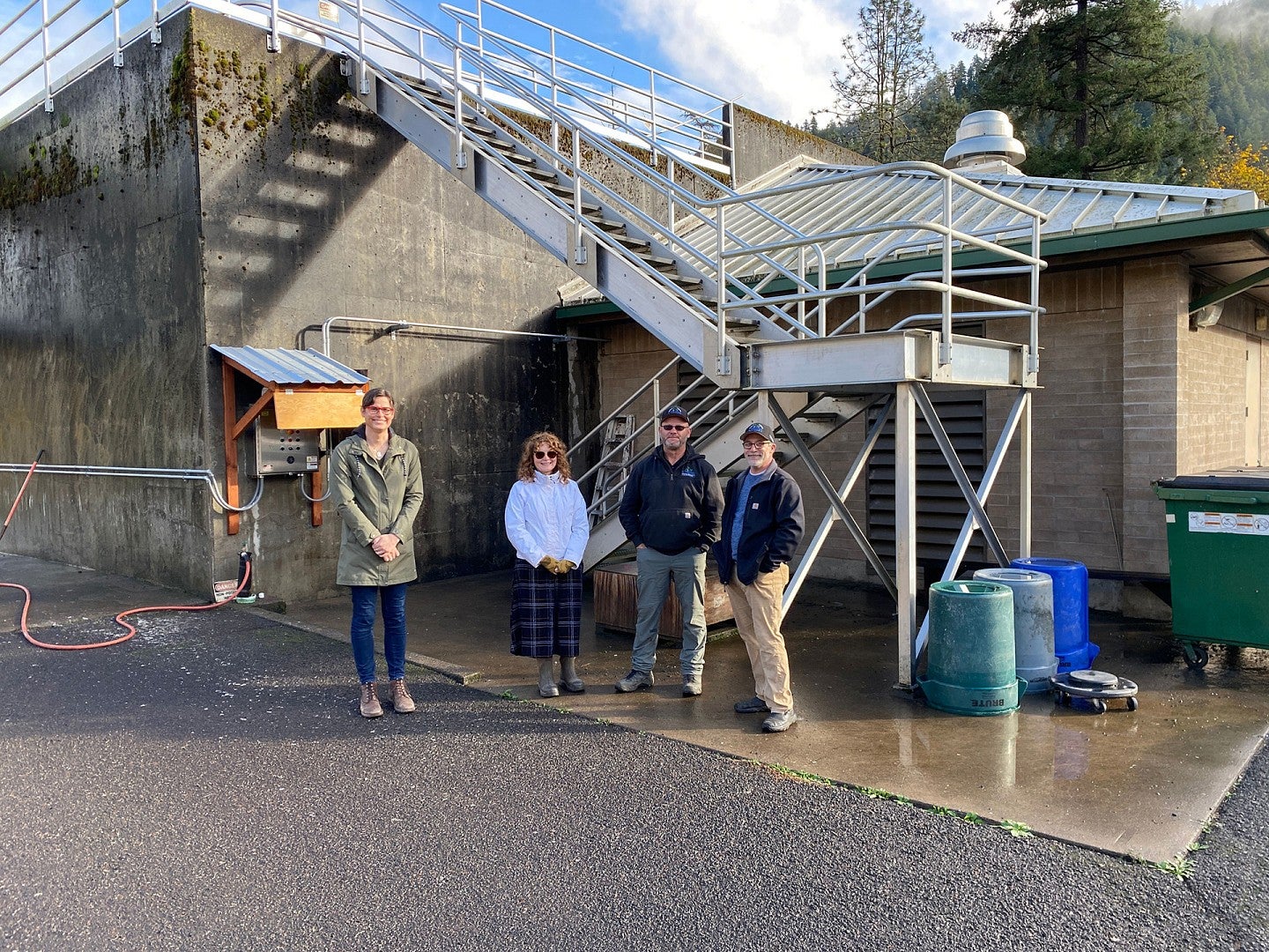 Four people stand and smile in front of wastewater treatment facility