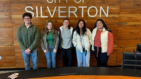 Group of students stand in front of wall that reads "City of Silverton"