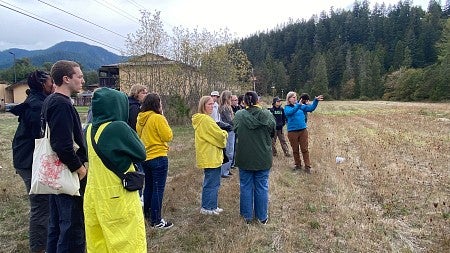 Group of students stand in field and listen to instructor