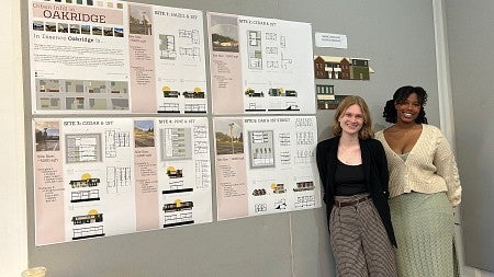 Two students smile next to large posters of their architecture project