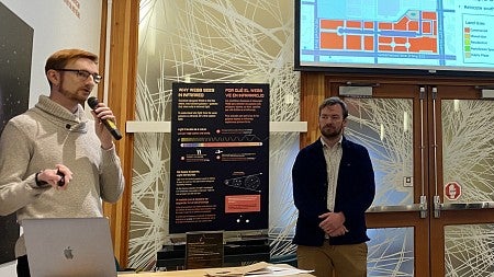Students stand in front of power point presentation with microphone
