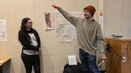 Two students stand in front of design charette materials and present their project