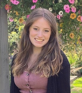 Headshot of Denali Herrick smiling against a tree with flowers