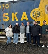 Six people stand in front of train and smile